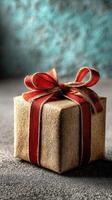Gift wrapped in burlap with a red bow placed on a textured surface in a cozy setting photo