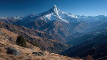 Snow-capped mountain peak rises majestically over the rugged valley landscape during clear blue sky conditions photo