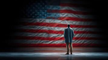 Person standing in front of a large American flag during a solemn moment of reflection in a dimly lit space photo