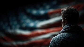 Man gazes thoughtfully towards a large American flag in a darkened environment, showcasing a moment of reflection and patriotism photo