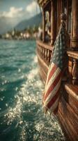 Vintage wooden boat with American flag draping over the side against a serene waterfront view and clear blue waters in the background photo