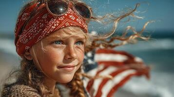 Young girl with sunglasses and a bandana smiles at the beach while holding an American flag on a sunny day photo