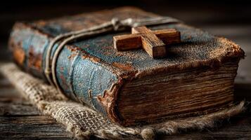 Old leather-bound book with wooden cross resting on burlap cloth in dim light photo