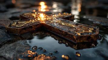 Golden cross rests on wet stones reflecting sunlight at dusk by a tranquil water source photo