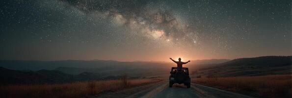 Stargazer celebrates the beauty of the Milky Way from a mountaintop road at dusk with arms raised in awe and wonder photo