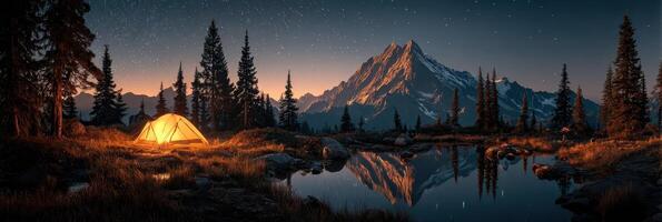 Tent lit by warm glow next to tranquil lake under starry sky in mountain landscape at dusk photo