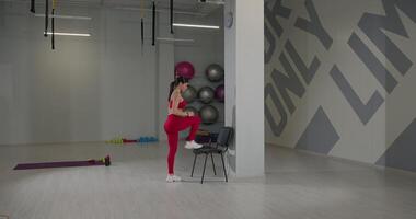 Woman performing exercise by stepping onto a chair in a modern gym environment during fitness routine video