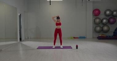 Girl performs shoulder and triceps stretch in a bright gym during an exercise session video