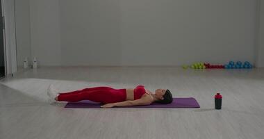 Girl performing abdominal exercises on a mat in a bright fitness studio during daytime for core strength and fitness video