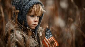 Young boy holding small American flag outdoors in fall season with muted colors surrounding him photo