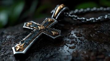 Exquisite close-up of an ornate cross pendant resting on a wet surface with lush greenery in the background photo