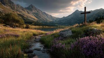 Serene lakeside landscape with mountains, flowers, and a wooden cross at sunset photo