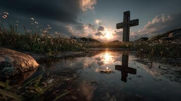 Sunset over a stone cross in a grassy field with reflections in a puddle photo