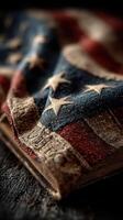 Old American flag draped over worn book with a rustic wooden background at sunset photo