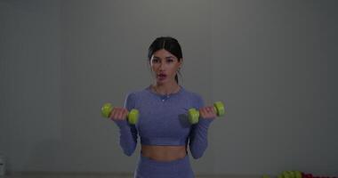 Sporty girl performs biceps exercises with dumbbells in modern gym setting video