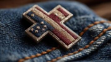 Decorative cross pin featuring American flag design rests on denim fabric in a warm light setting photo