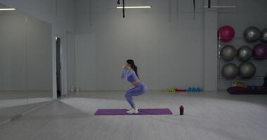 Sporty girl performs squats with dumbbell press in modern gym setting during a workout session video