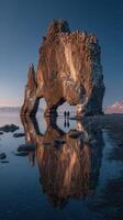 Two people exploring a giant rock formation by calm water at sunset in Iceland photo