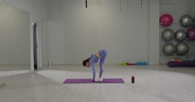 Girl performs a deep stretch while bending in a spacious gym during a fitness routine video