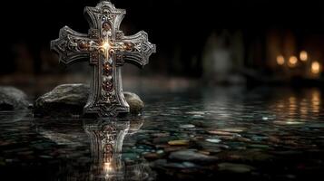 Silver cross resting on stones in reflective water, illuminated by soft candlelight in a dimly lit setting photo