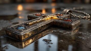 Silver crucifix with gemstones reflecting light on a wet surface in a dimly lit space photo