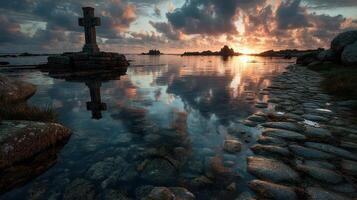 Stunning sunset reflection over a tranquil waterway with a stone cross and rocky shoreline in a coastal landscape photo