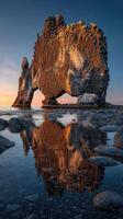 Stunning rock formation at sunset near the shoreline with reflections in still water photo