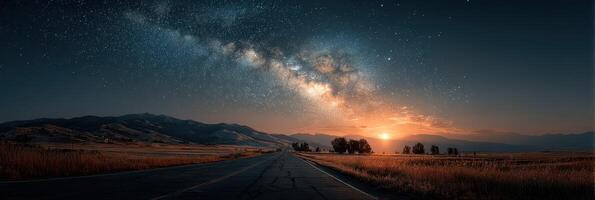 Starlit night sky over an empty road with mountains and a glowing sunset in the distance photo