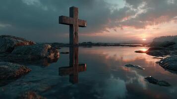 Stone cross stands tall over tranquil water at sunset near rocky shoreline photo