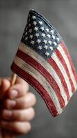 Hand holding a small fabric American flag against a neutral background in celebration of patriotism photo