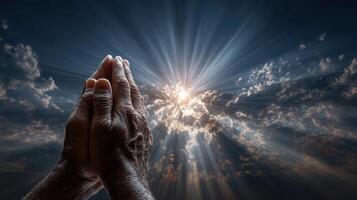 Hands raised in prayer against a dramatic sky filled with clouds and rays of sunlight during a serene moment of reflection photo