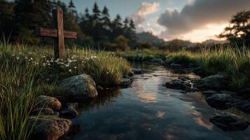 Tranquil stream with wooden cross surrounded by grass and wildflowers at sunset in a serene landscape photo