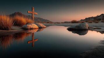 Serene landscape at dusk with a wooden cross reflecting in still water beside rocks and grass photo