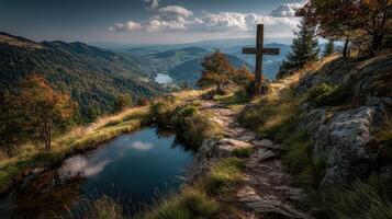 Mountain trail leading to a cross overlooking a valley with a lake in the distance during a clear day in autumn photo