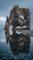 Giant rock formation at Hvitserkur reflects in calm water during twilight in Iceland photo