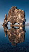 Majestic rock formation in calm waters reflecting stunning landscape during sunset in Iceland photo