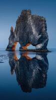 Stunning rock formation in a calm sea with reflective surface at sunset in Iceland photo