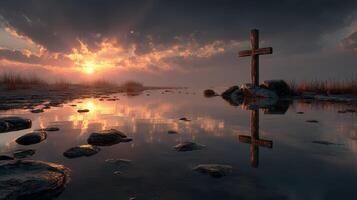 Sunset reflected in water with a cross standing on rocky shore during dusk photo