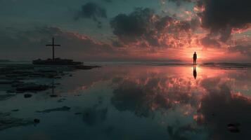 Beautiful sunset illuminating a solitary figure by a cross on the shore with reflections in calm water photo