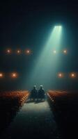 Two figures sit in a dimly lit theater, illuminated by a single spotlight from above during an intimate moment photo