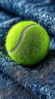 Bright green tennis ball resting on a textured blue denim fabric background in a close-up shot capturing vibrant colors photo