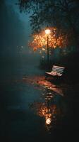 Evening stroll in a misty park with a glowing lamp and autumn leaves on a wet bench photo