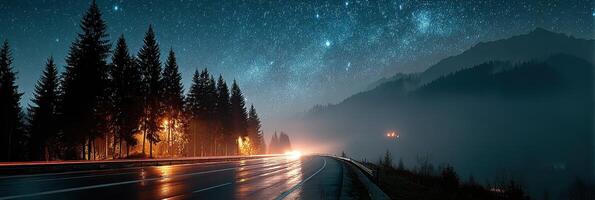 Starry night over a winding road in the mountains with glowing lights and misty trees photo