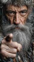 Elderly man with a gray beard pointing directly at the viewer in a dramatic portrait setting photo