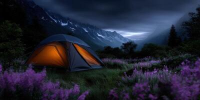 Beautiful camping site at dusk in the mountains with glowing tent and blooming wildflowers photo