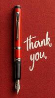 Elegant red fountain pen arranged beside a handwritten thank you note on a textured red background photo