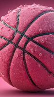Close-up view of a textured pink basketball surrounded by water droplets on a vibrant pink background photo