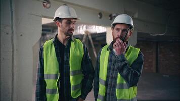 caucasiano eletricistas supervisores construtores dentro construção rapazes operários conversa defeituoso rádio conjunto problema erro quebrado dispositivo homens engenheiros Socorro empreiteiros Falando trabalhando walkie talkie trabalho em equipe Construir video