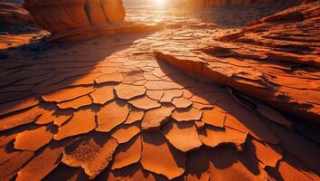 Dry Cracked Earth at Sunset with Golden Sunlight and Rock Formations photo