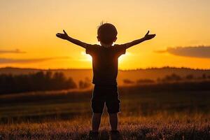 Child silhouetted at sunset, arms outstretched photo
